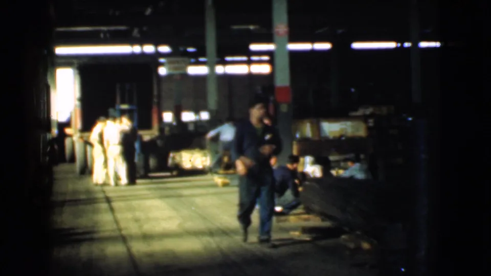 In 1939 Cleveland footage, a uniformed worker moves down a shadowed warehouse causeway while other workers and materials appear behind him.