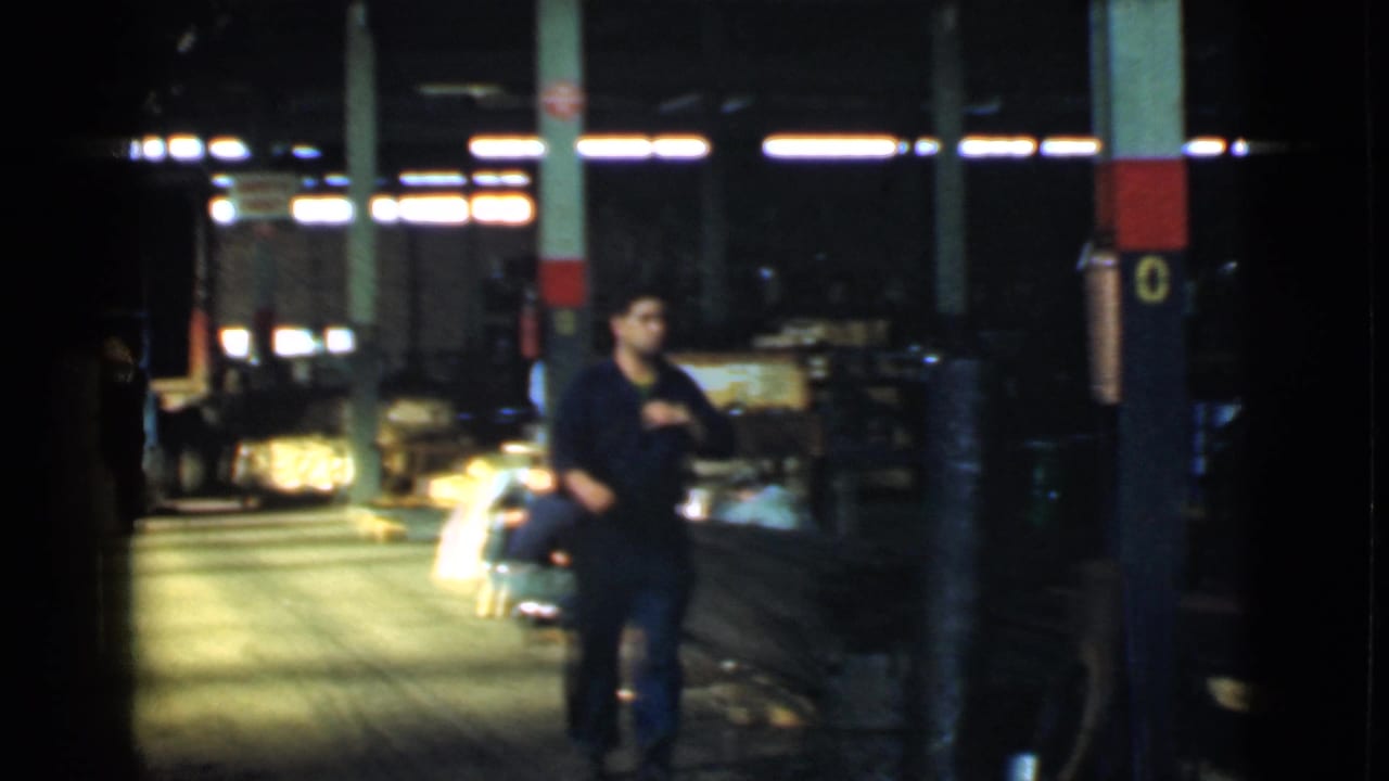 Uniformed worker passes a painted column inside a dark warehouse space.