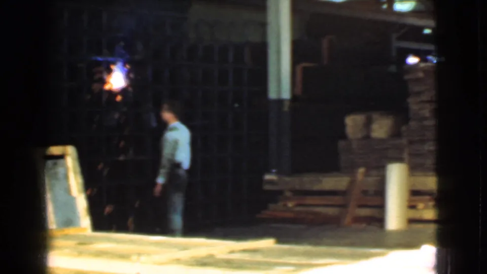 1939 Cleveland industrial yard frame with a worker beside an active welding flash and lumber stacks nearby.