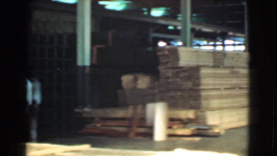 1939 Cleveland industrial yard frame with a partly visible worker and large stacks of lumber beside a dark gate.