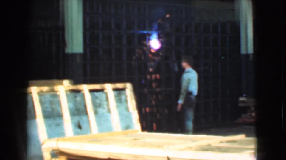 In the supplied 1939 Cleveland clip, a man watches a bright welding torch inside a dim warehouse with wooden crates and framing.