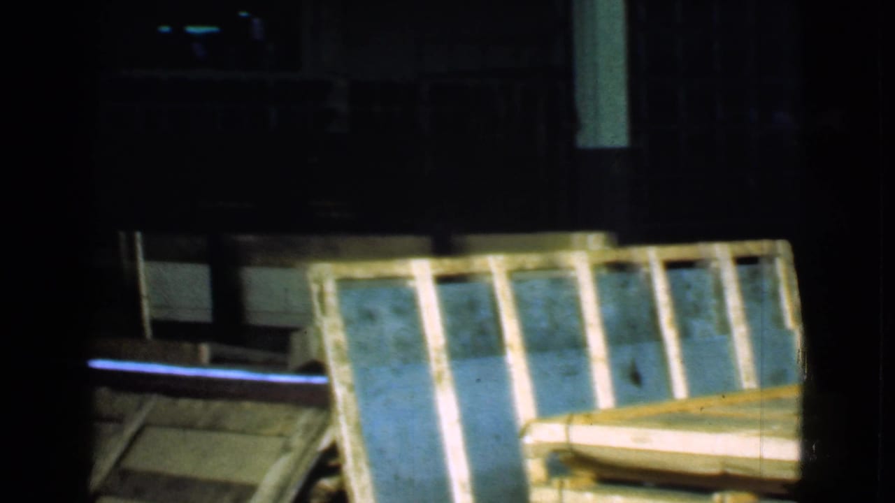Wooden crate panels fill a dark warehouse area with columns and shelving behind them.