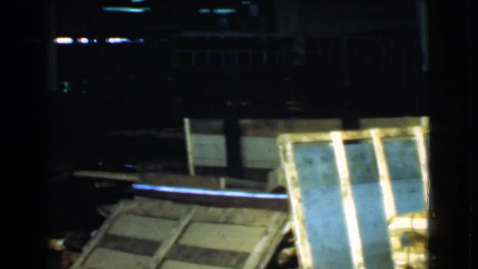 Leaning wooden frames, crates, and lumber-like materials are seen in a dark 1939 Cleveland warehouse setting.