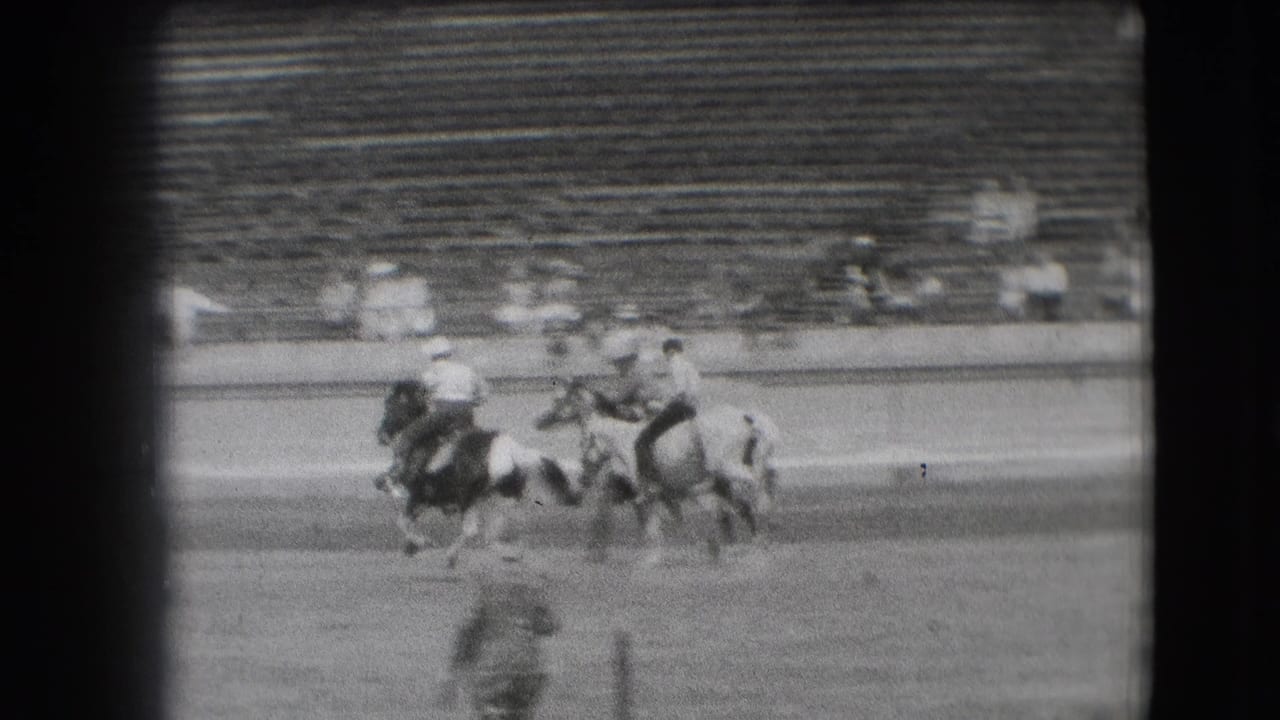 Mounted riders cluster in a dirt arena with stadium bleachers behind them.