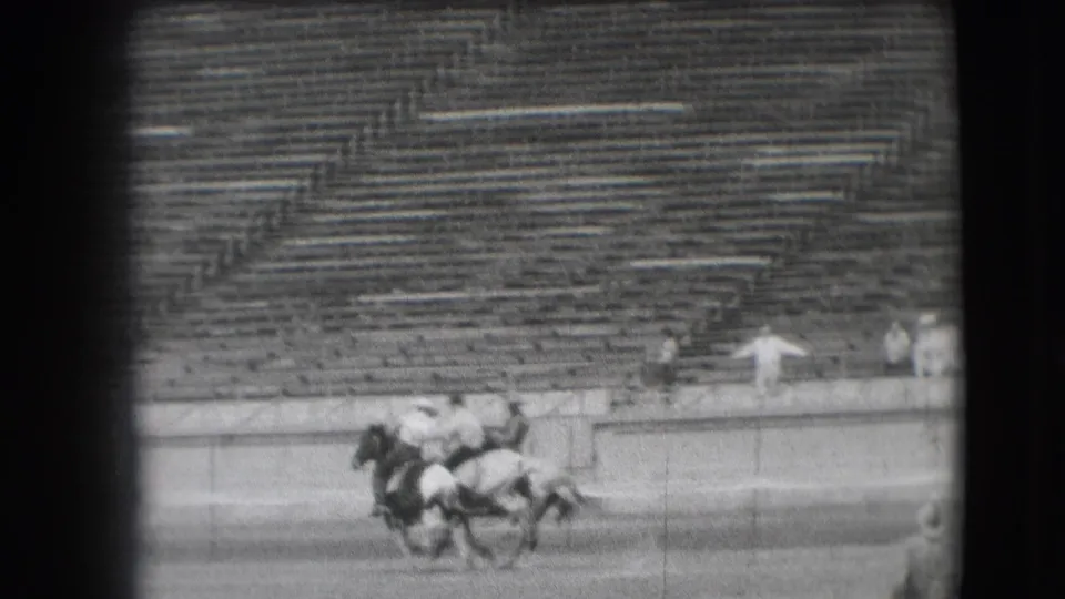 In the Denver arena, riders on horseback move together across the dirt field with rows of stadium seating in the background.