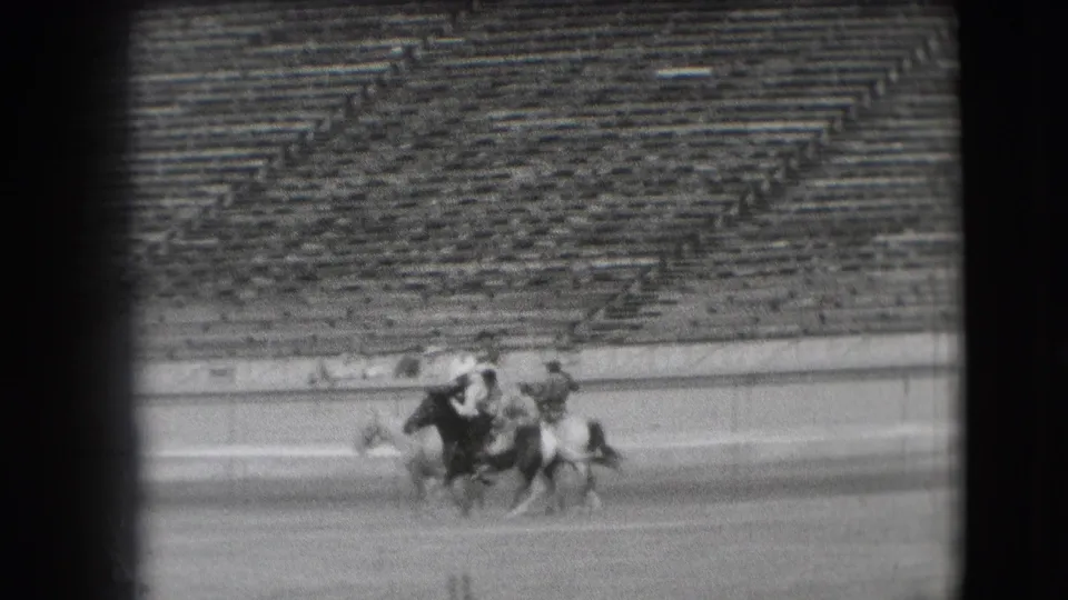 Cowboys on horseback appear to bunch or turn during a maneuver in the 1941 Denver rodeo arena, with bleachers filling the background.