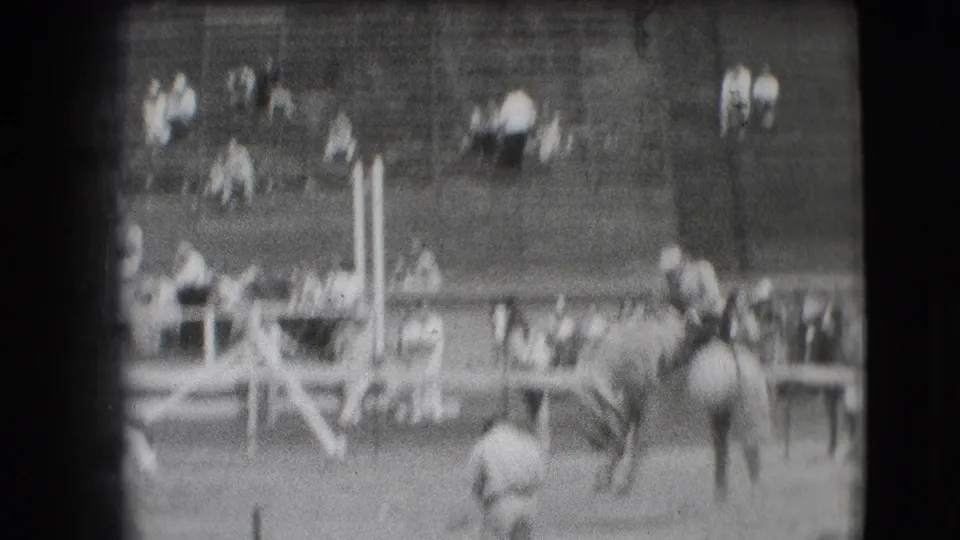 1941 Denver rodeo frame showing a rider on a bucking horse near rail fencing, with spectators seated in the background.