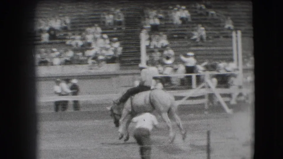 1941 Denver rodeo view of a horse mid-buck with the rider leaning forward and a man standing in the arena nearby.