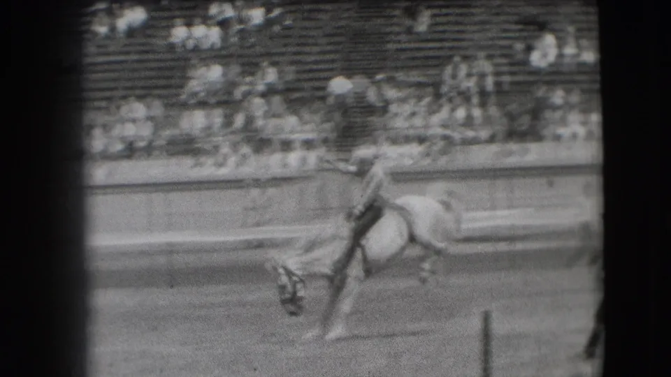 1941 Denver rodeo frame with the horse pitching forward, rider still mounted, and spectators watching from tiered seating.