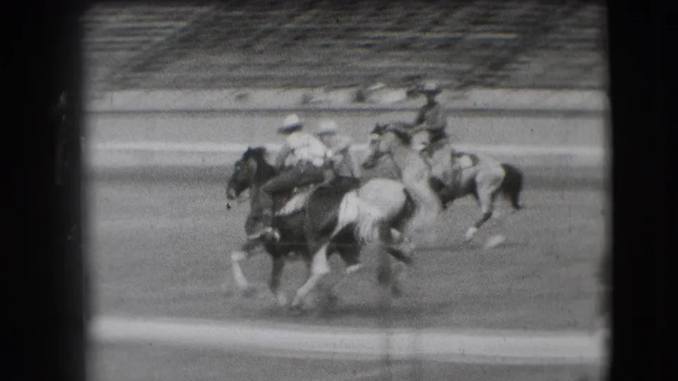 A group of mounted riders moves through the Denver rodeo arena, partly blurred by the 8mm motion.
