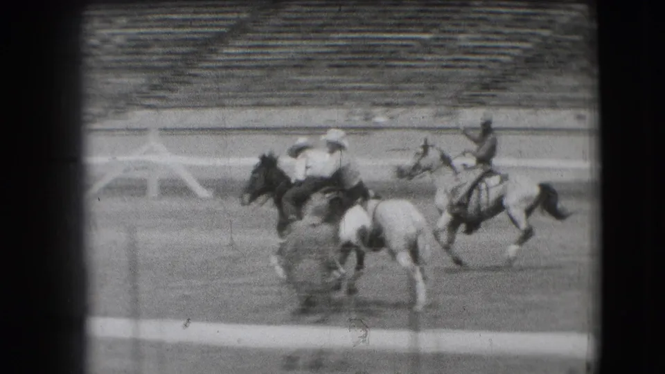 1941 Denver home-movie frame showing riders on horseback at a stadium track, with one rider appearing to fall as other horses move past.