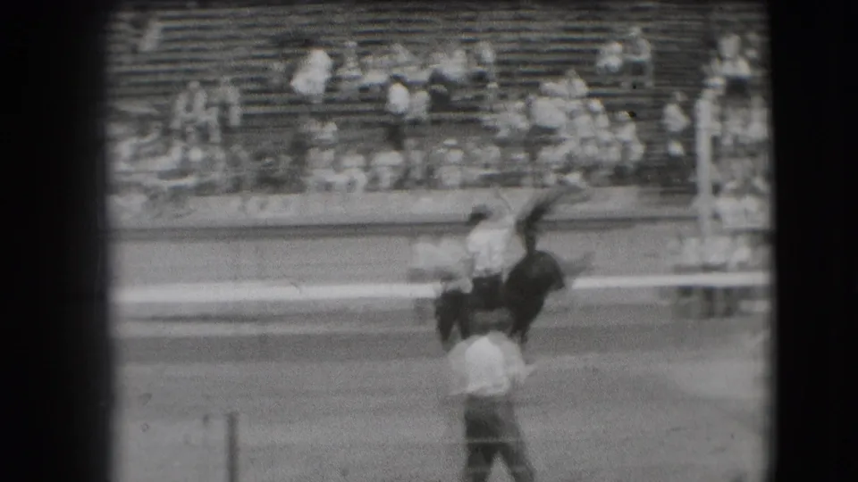 1941 Denver stadium-track frame with a horse and rider in motion, a foreground spectator, railings, and seated spectators behind.