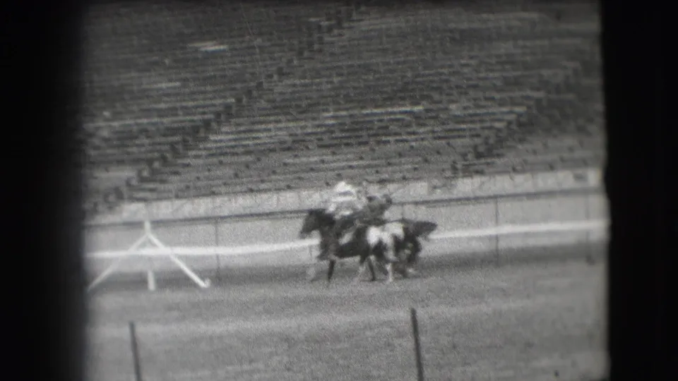 Clustered polo riders and horses move along the arena edge, with empty tiered seating behind them in the Denver 1941 home-movie footage.