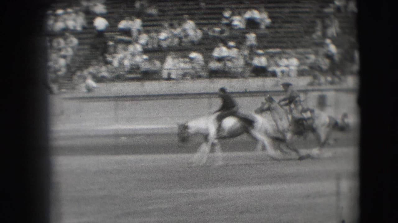 1941 Denver arena view with a mounted rider and horse moving past tiered spectator seating in black-and-white 8mm footage.