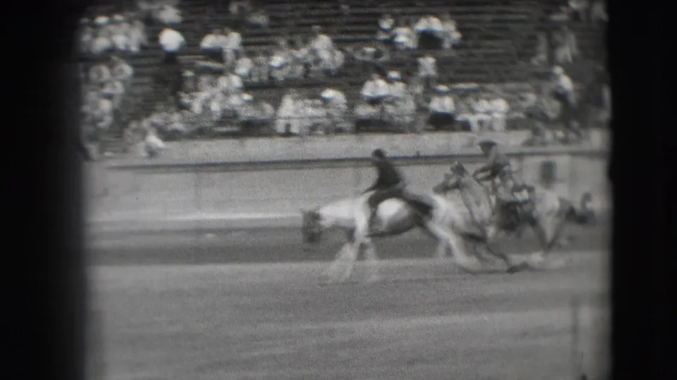 1941 Denver arena view with a mounted rider and horse moving past tiered spectator seating in black-and-white 8mm footage.