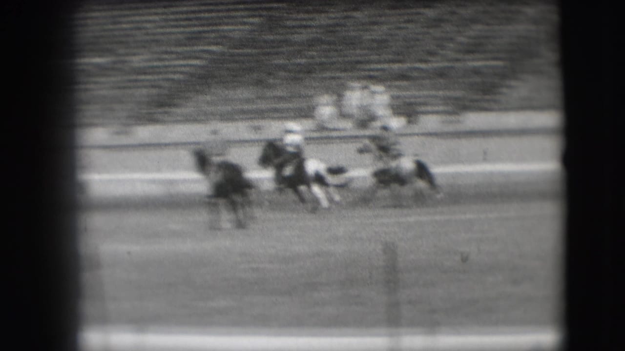 In supplied 1941 Denver rodeo footage, a cowboy rides a bucking pinto horse as bleachers blur in the background.