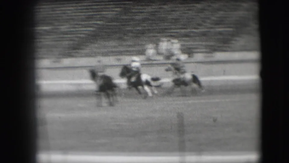 In supplied 1941 Denver rodeo footage, a cowboy rides a bucking pinto horse as bleachers blur in the background.