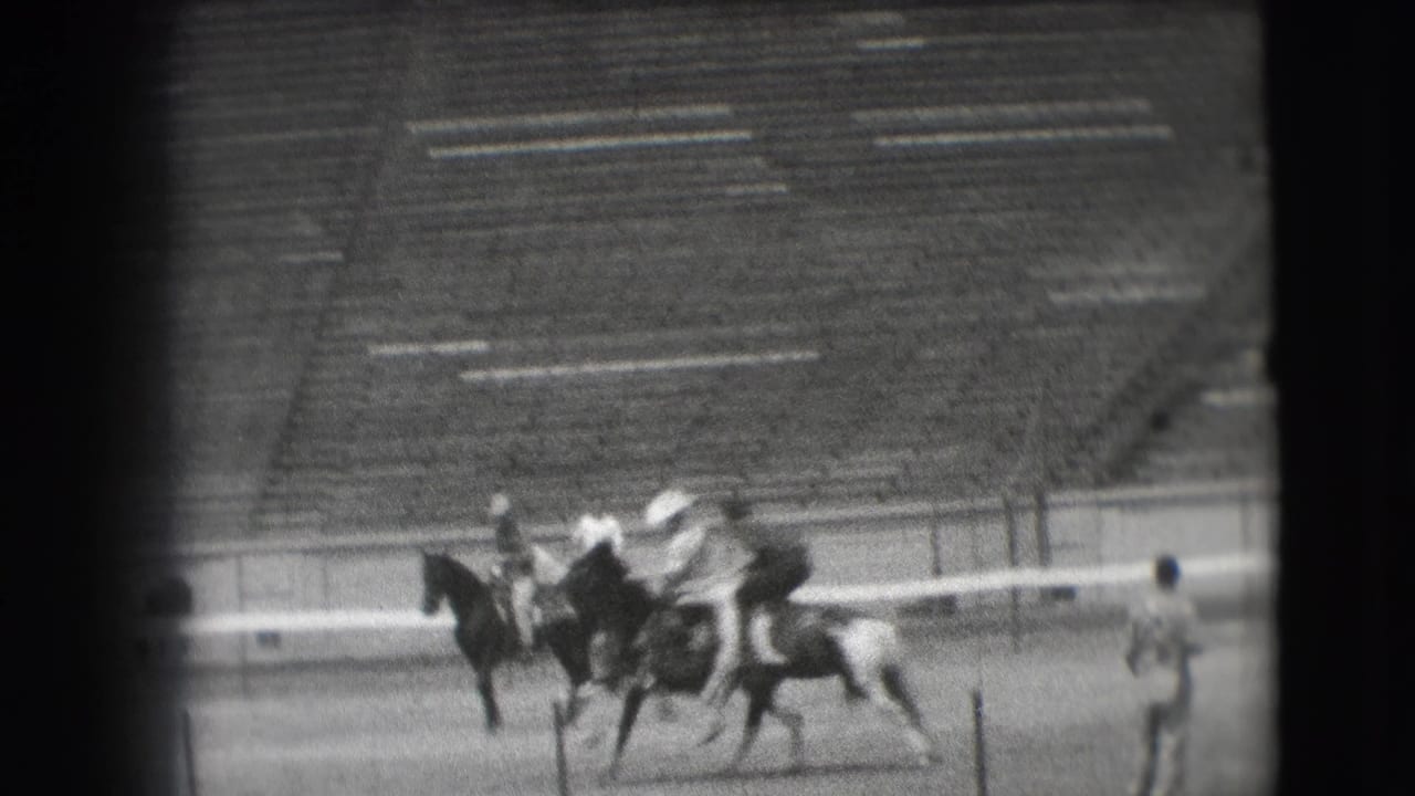 Riders on horses move across a stadium field with empty bleachers behind them.