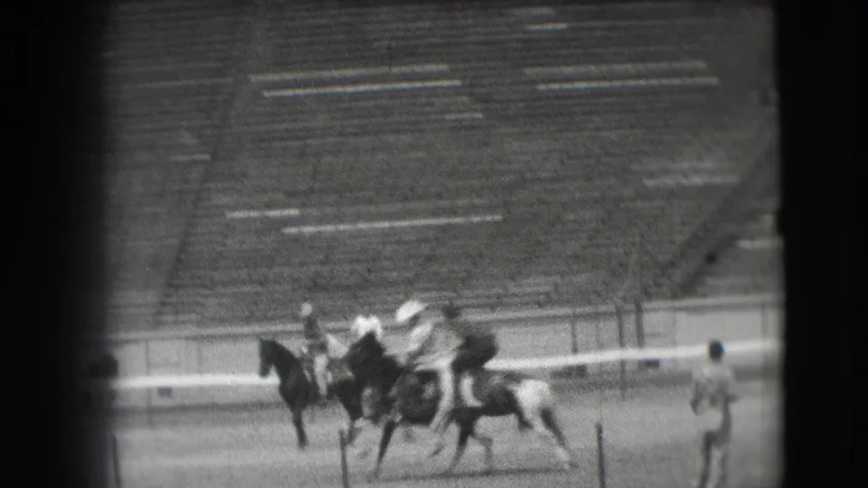 1941 Denver home-movie frame showing riders and horses crossing a stadium field during equestrian practice.