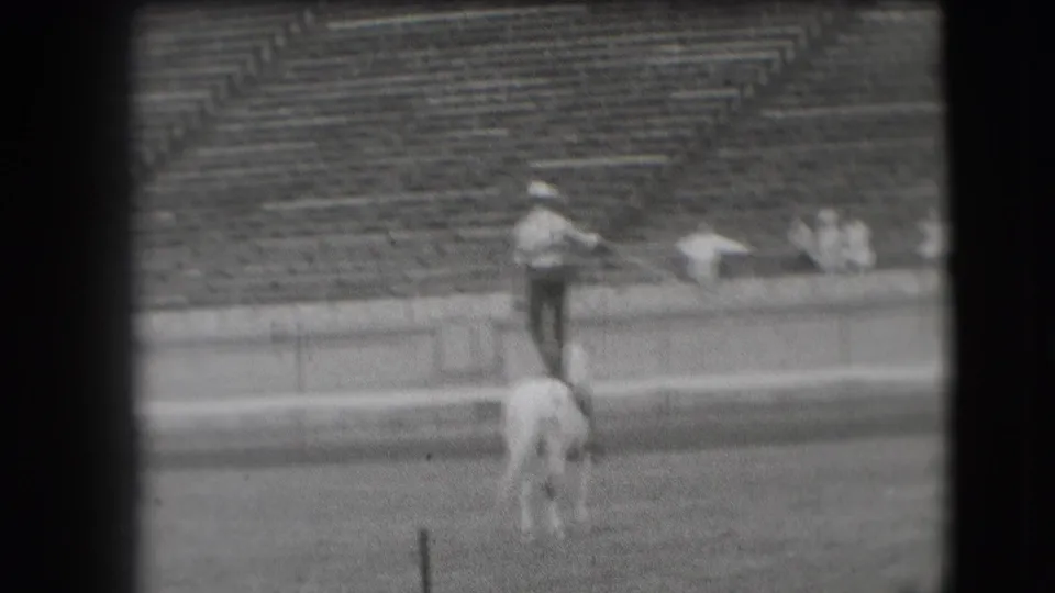 Denver 1941 home-movie frame showing an equestrian stunt rider balancing on a white horse in a stadium.