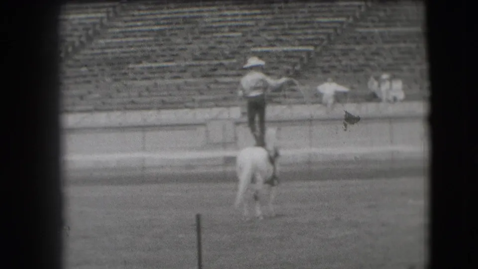 Black-and-white 8mm frame shows the rodeo performer spinning a lasso from atop a white horse in Denver.