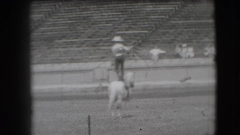 In 1941 Denver rodeo footage, a cowboy in a light hat stands on a white horse before stadium bleachers.