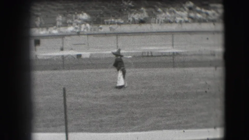 1941 Denver rodeo frame showing a cowboy in the arena handling a lasso, with low fencing and stadium seating in the background.