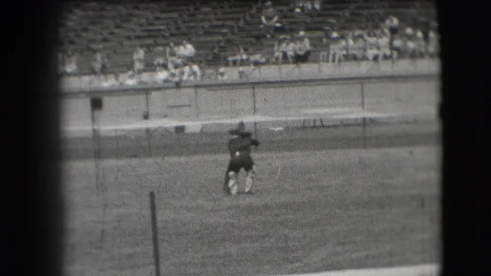 A cowboy-style performer appears to bend or pivot on a Denver stadium field, with scattered spectators seated behind the barrier.