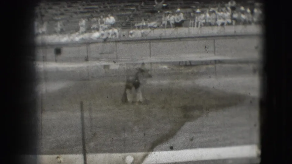 Motion blur from the 8mm footage shows the costumed dancer moving across the grassy field at the Denver stadium event.