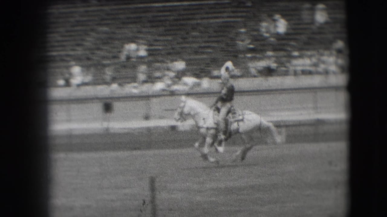 A cowboy on a light-colored horse passes below the stands during the 1941 Denver rodeo, captured with soft focus and film grain.