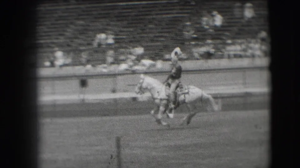A cowboy on a light-colored horse passes below the stands during the 1941 Denver rodeo, captured with soft focus and film grain.