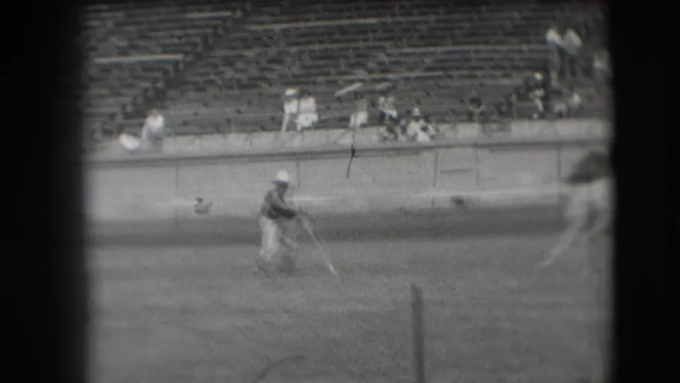 A ground participant stands in the rodeo arena as the mounted rider exits near the right edge, with stadium seats and spectators behind.