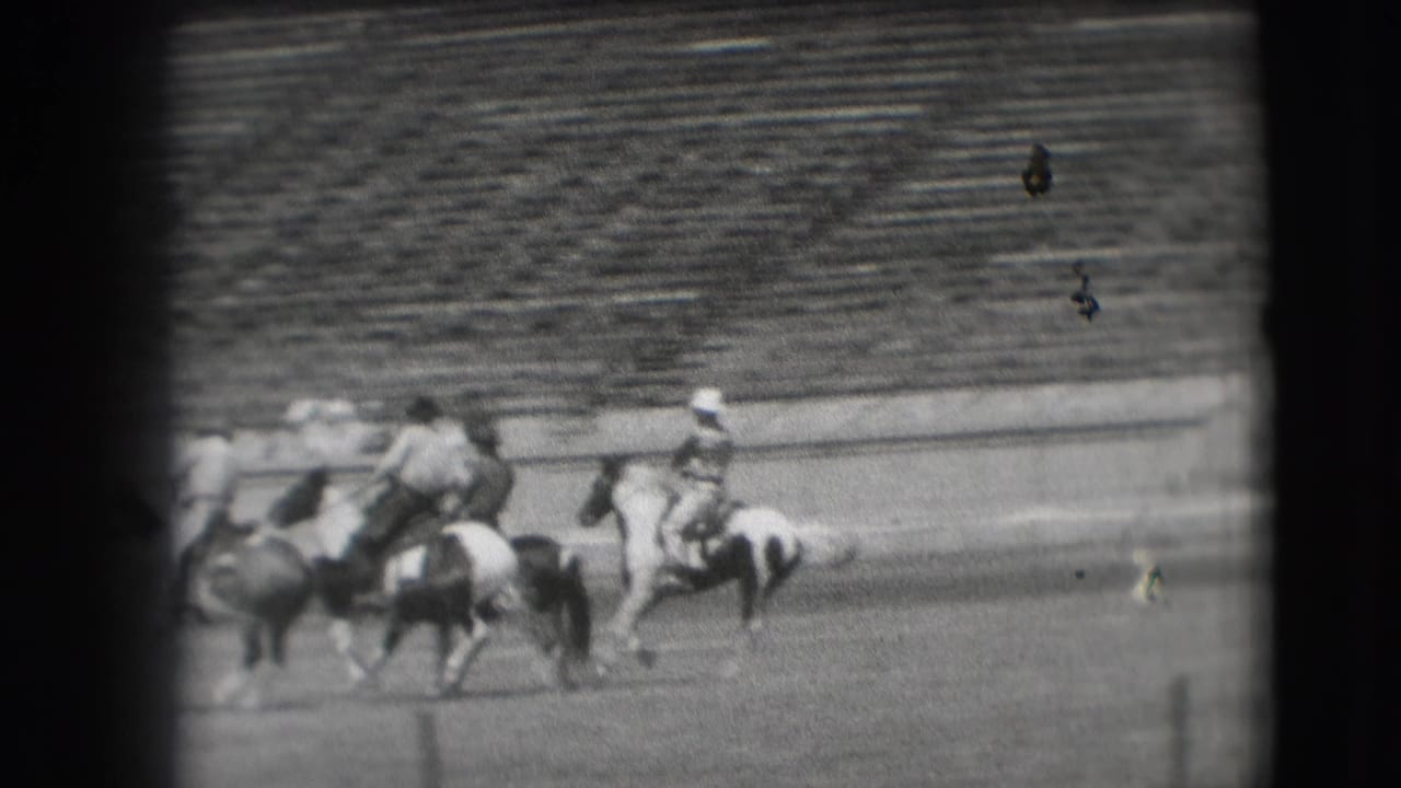 Cowboys on horseback appear clustered during a Denver rodeo sequence, with stadium bleachers visible in the background.