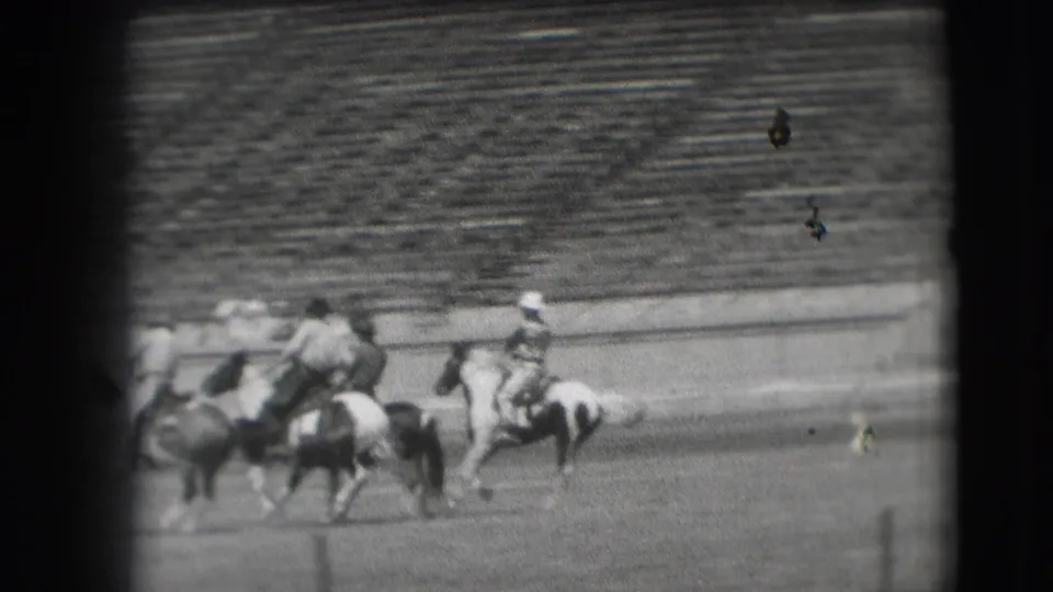 Cowboys on horseback appear clustered during a Denver rodeo sequence, with stadium bleachers visible in the background.