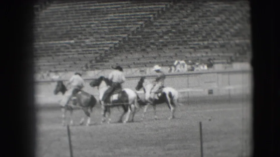 1941 Denver rodeo home-movie frame with three riders on horses crossing the field before rows of spectators.