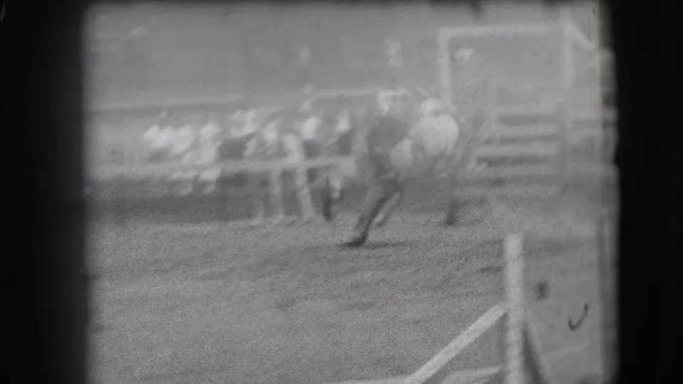 In Denver archival 8mm footage, a rider appears on a bucking horse inside a rodeo arena with spectators beyond the rail.