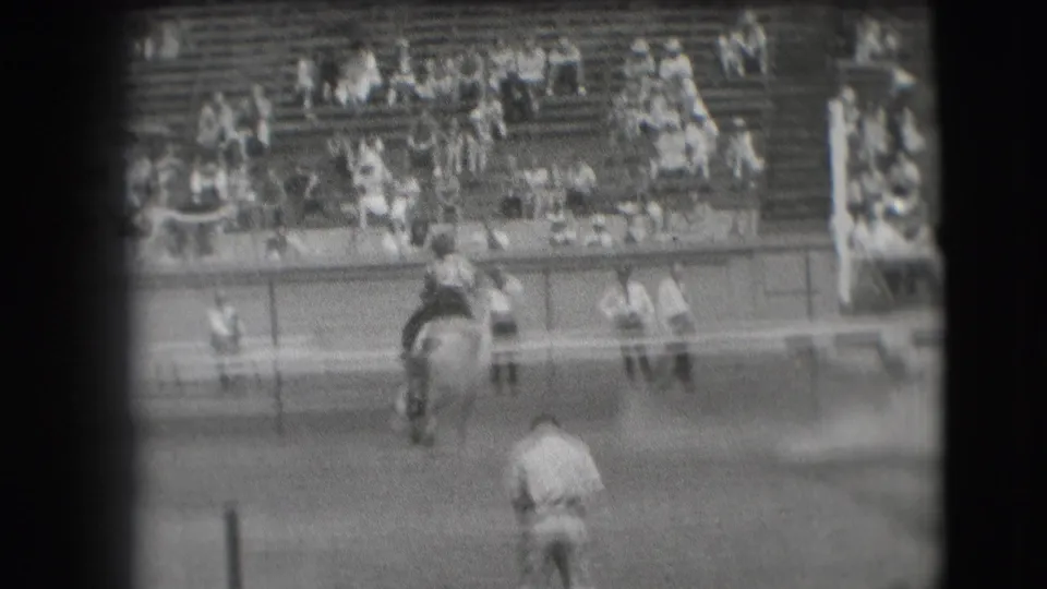 From a spectator angle, the rider and horse are seen lower in the frame while the bleachers and arena rail fill the background.