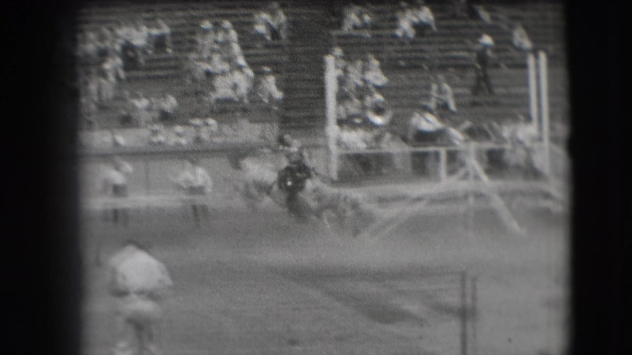 Rider on horseback moving through a dusty rodeo arena with spectators in the grandstand.