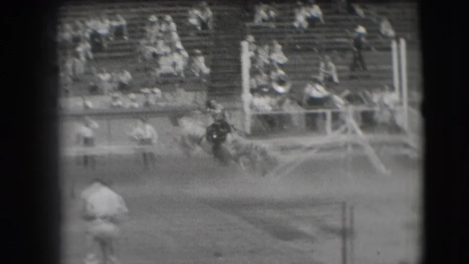 1941 Denver rodeo home-movie frame showing a mounted rider in a dirt arena before blurred grandstand spectators.