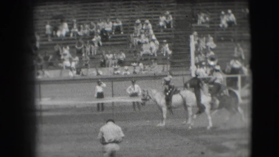 1941 Denver rodeo frame showing mounted riders in the dirt arena with spectators spread across wooden bleachers.