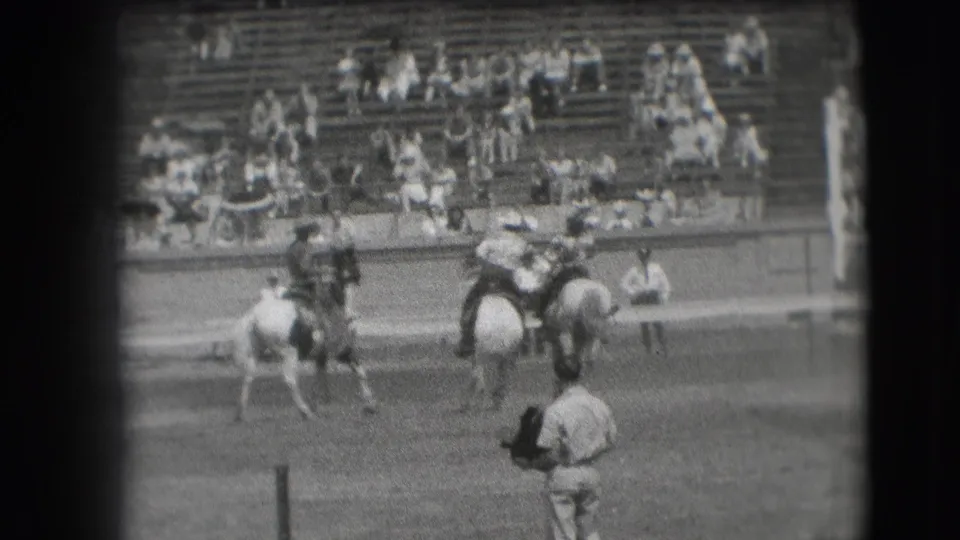 1941 Denver rodeo home-movie frame showing mounted riders in an outdoor arena with bleacher spectators in the background.