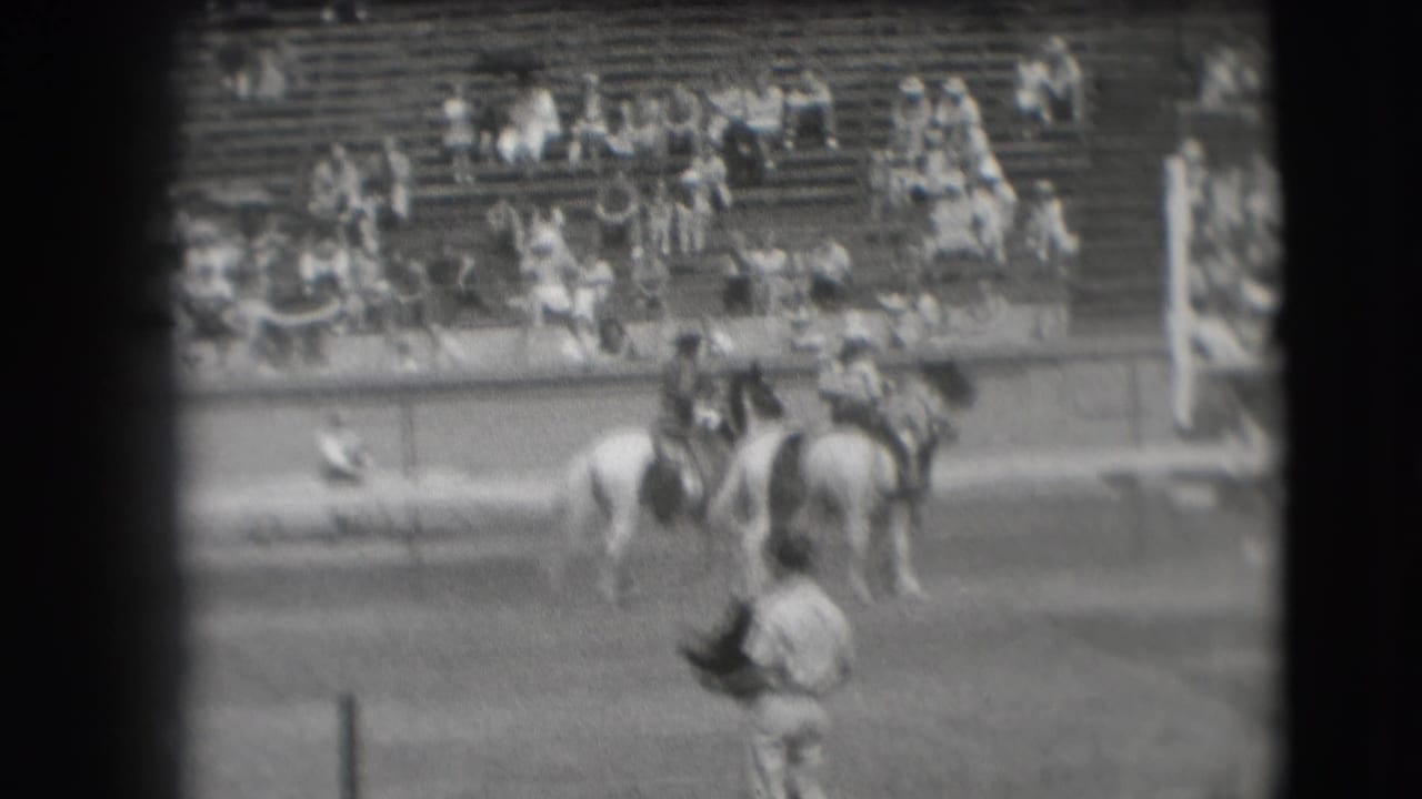 1941 Denver rodeo frame with multiple riders and horses clustered in front of outdoor bleachers.
