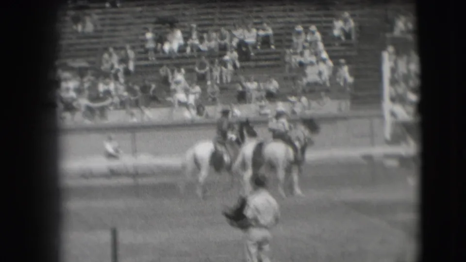1941 Denver rodeo frame with multiple riders and horses clustered in front of outdoor bleachers.