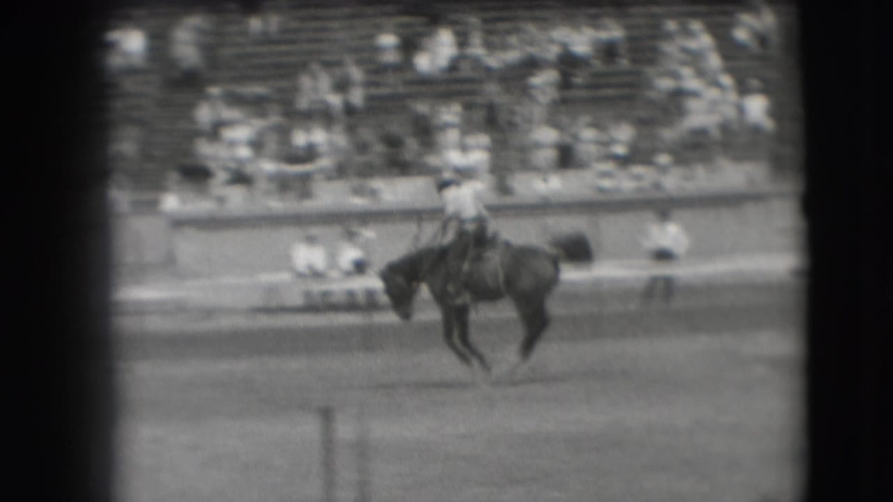 1941 Denver rodeo frame showing a rider on a bucking horse crossing the arena before distant bleachers.