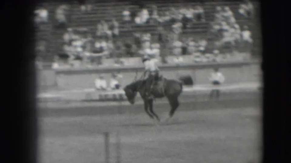 1941 Denver rodeo frame showing a rider on a bucking horse crossing the arena before distant bleachers.