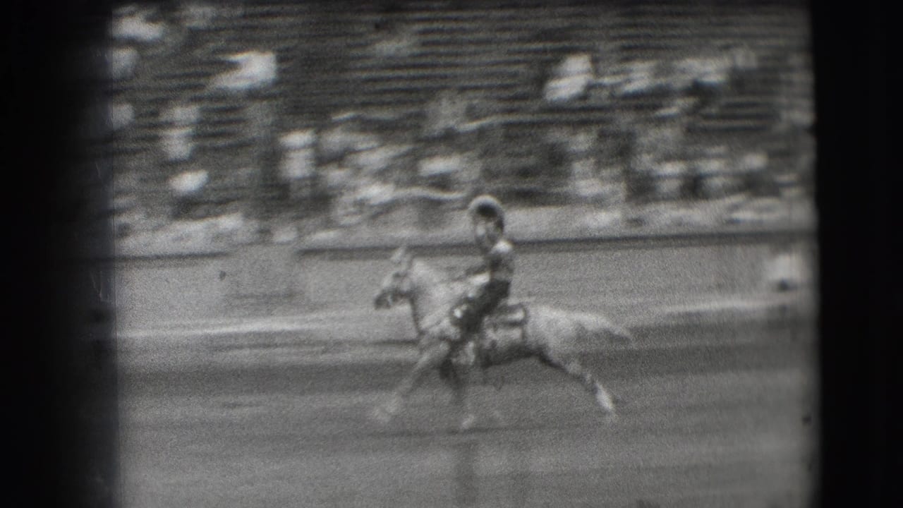 The rodeo rider continues across the dirt arena in the 1941 Denver home movie, with blurred bleachers and spectators behind the action.