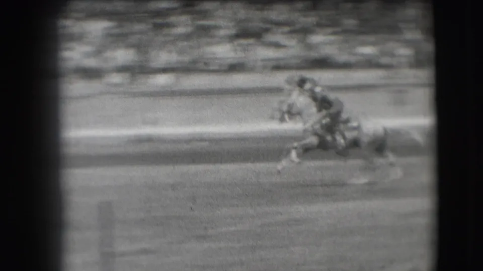 Near the end of the clip, the rider is low against the moving horse as the Denver rodeo arena and bleacher crowd blur in the background.