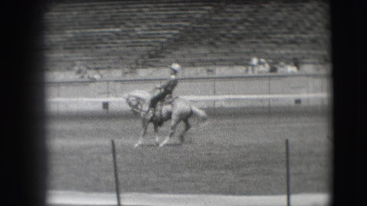 The rodeo competitor appears mid-motion on horseback in the 1941 Denver arena, filmed from a distant spectator viewpoint.