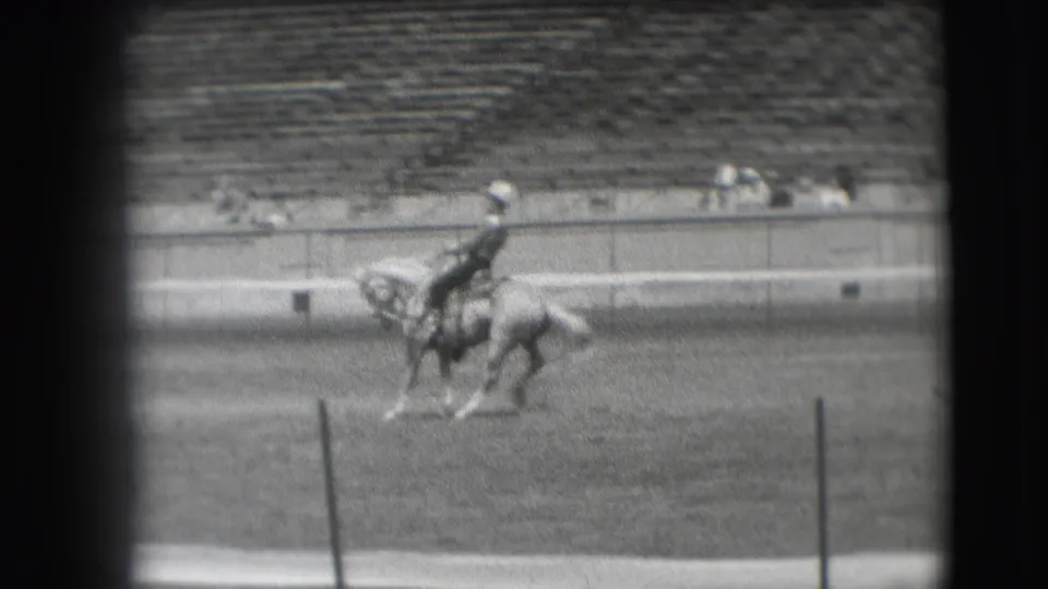 The rodeo competitor appears mid-motion on horseback in the 1941 Denver arena, filmed from a distant spectator viewpoint.