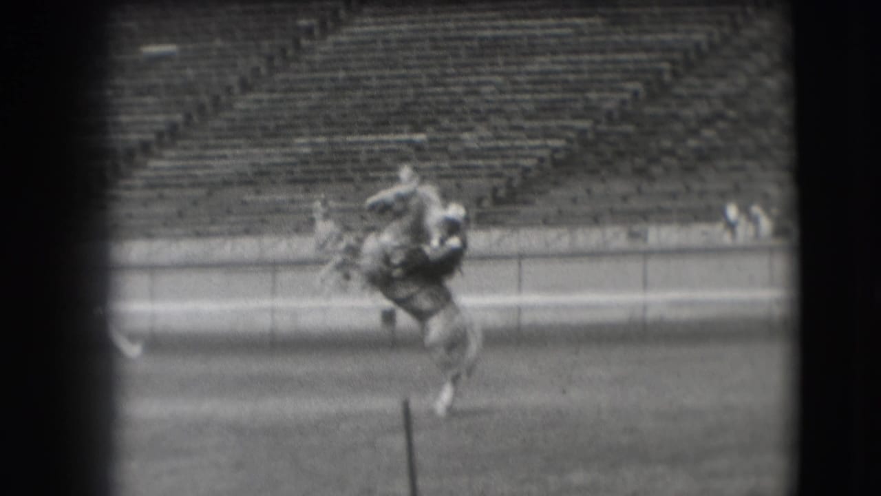 A rider on horseback continues across the Denver rodeo arena, partially framed by dark film edges and a foreground post.